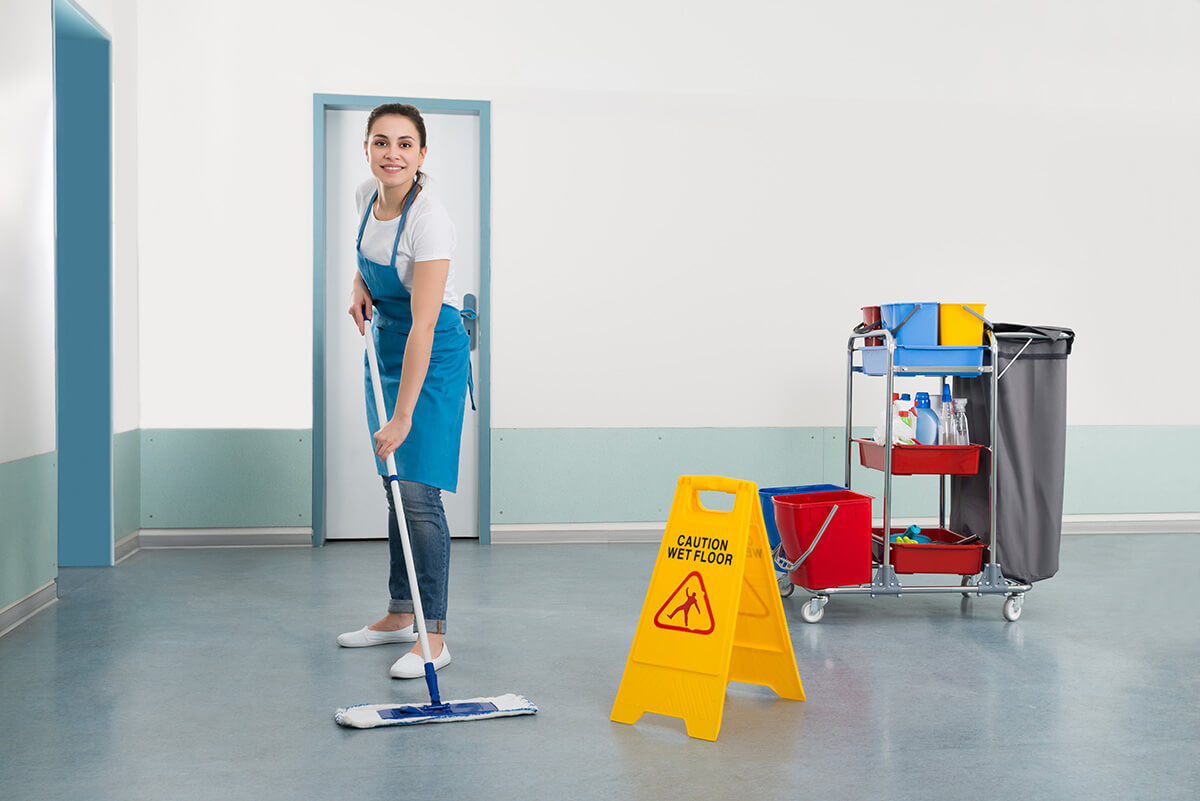 A female convenience store employee mops the floor outside a public restroom.
