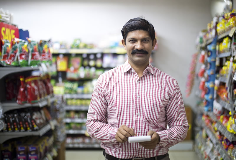 A man holding a notepad stands in aisle of a convenience store.