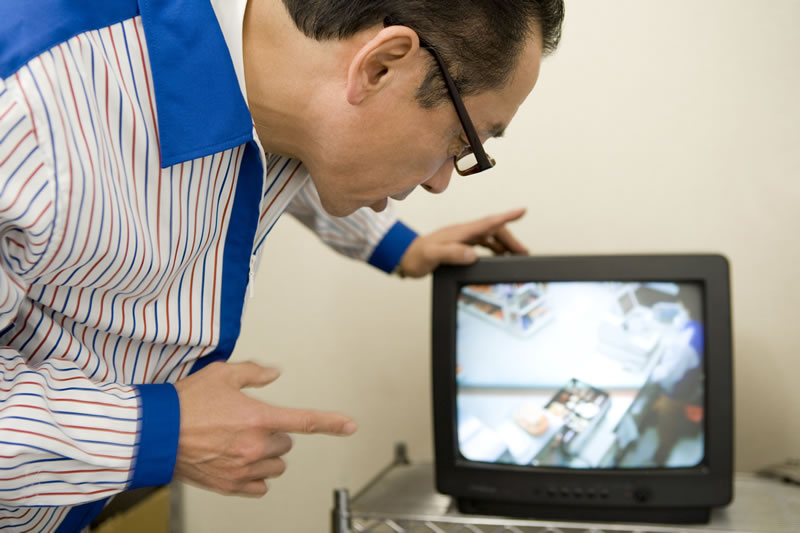A man bends over to look at security camera footage on a small video monitor.
