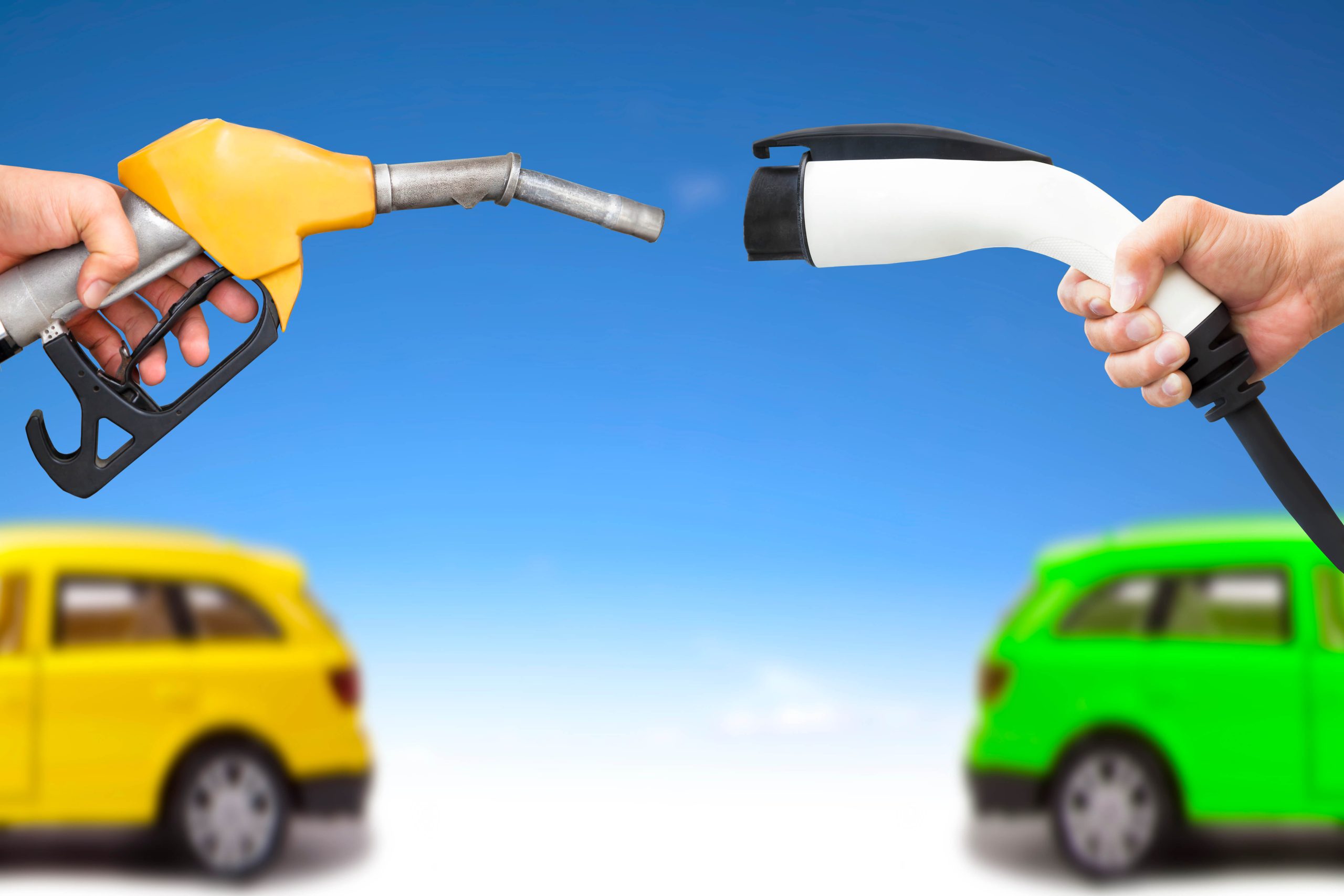 A hand holding a gasoline pump nozzle faces another hand that holds an electric vehicle charging port.